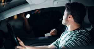 Man in a car, looking out the window at an officer with a flashlight